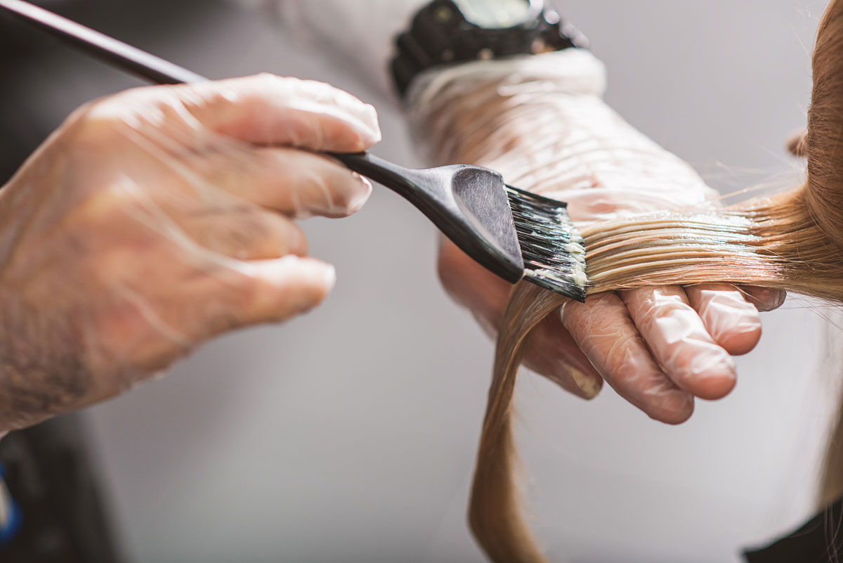 A close-up of a hairdresser’s hands dying a woman’s hair.