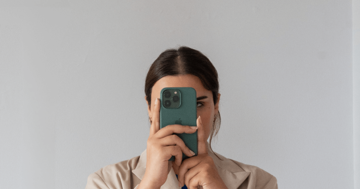 a woman is facing the camera holding aa green iPhone up to her face so it is covering half her face.